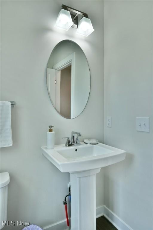 half bath featuring baseboards, toilet, and a sink