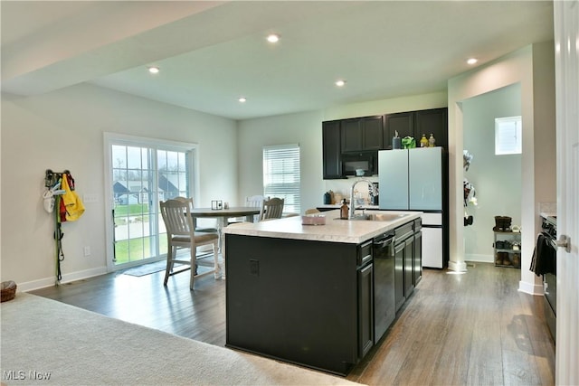kitchen with a center island with sink, freestanding refrigerator, wood finished floors, dishwasher, and light countertops