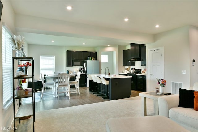 kitchen featuring a sink, open floor plan, light wood-style floors, light countertops, and black appliances