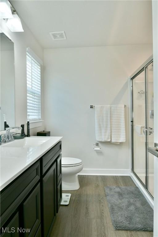 bathroom with toilet, wood finished floors, visible vents, and a stall shower