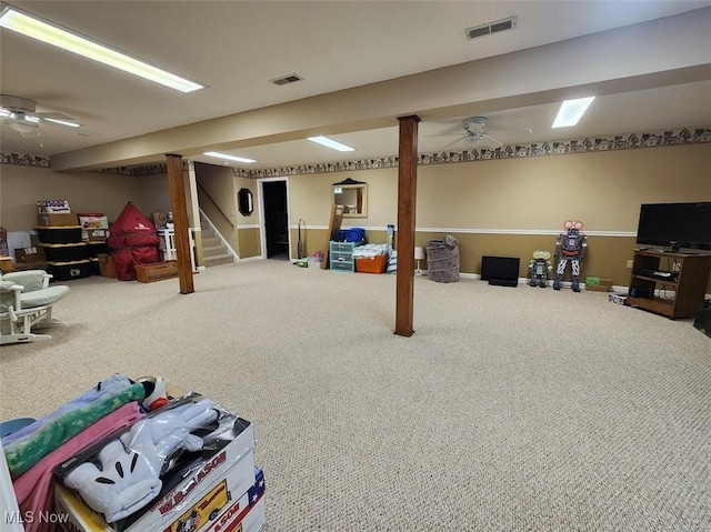 finished basement with stairway, a ceiling fan, visible vents, and carpet