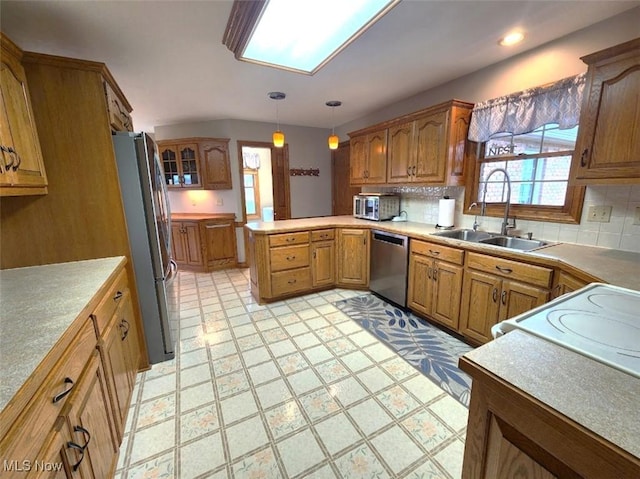 kitchen with a peninsula, a sink, tasteful backsplash, brown cabinetry, and appliances with stainless steel finishes