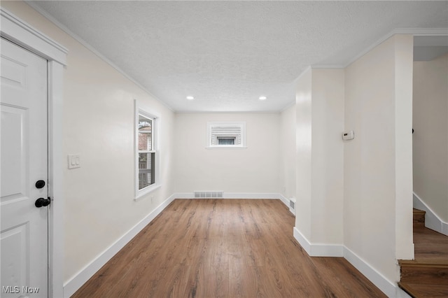 below grade area featuring wood finished floors, a textured ceiling, baseboards, ornamental molding, and visible vents