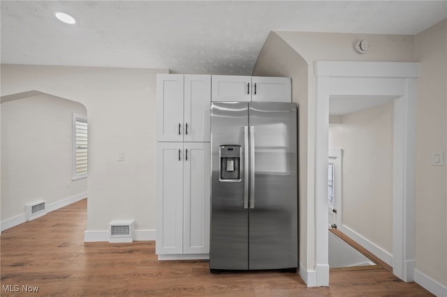 kitchen featuring white cabinets, stainless steel fridge, wood finished floors, and visible vents