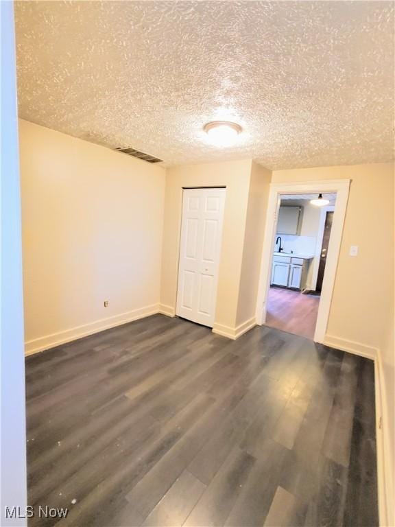 spare room with a textured ceiling, visible vents, baseboards, and dark wood-type flooring