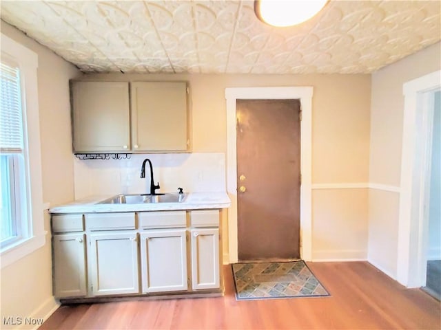 kitchen featuring light wood finished floors, a sink, baseboards, and light countertops