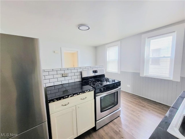 kitchen featuring white cabinetry, stainless steel appliances, a wainscoted wall, and light wood finished floors
