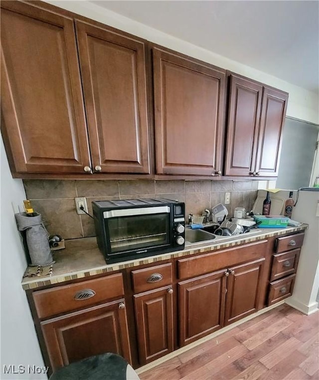 kitchen with a toaster, light countertops, decorative backsplash, and light wood-style floors