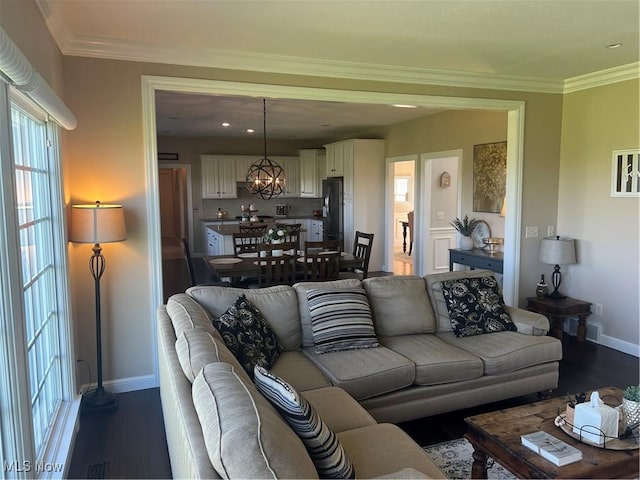 living area featuring crown molding, baseboards, dark wood-style flooring, and an inviting chandelier