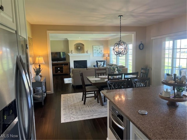 kitchen featuring stainless steel fridge with ice dispenser, dark wood-type flooring, decorative light fixtures, dark stone counters, and a fireplace