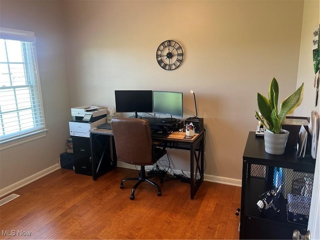office space with baseboards, wood finished floors, visible vents, and a wealth of natural light