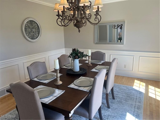 dining room with an inviting chandelier, crown molding, wood finished floors, and a decorative wall