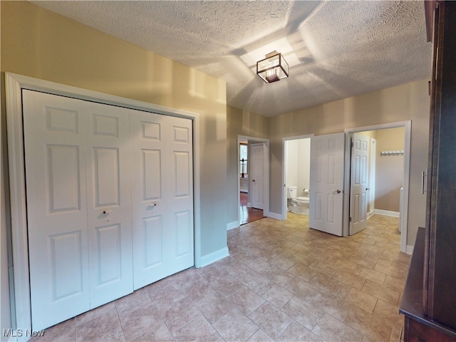 unfurnished bedroom featuring a closet, a textured ceiling, baseboards, and connected bathroom