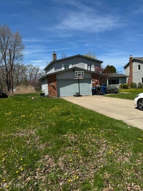 view of side of property with a chimney, concrete driveway, a garage, brick siding, and a yard