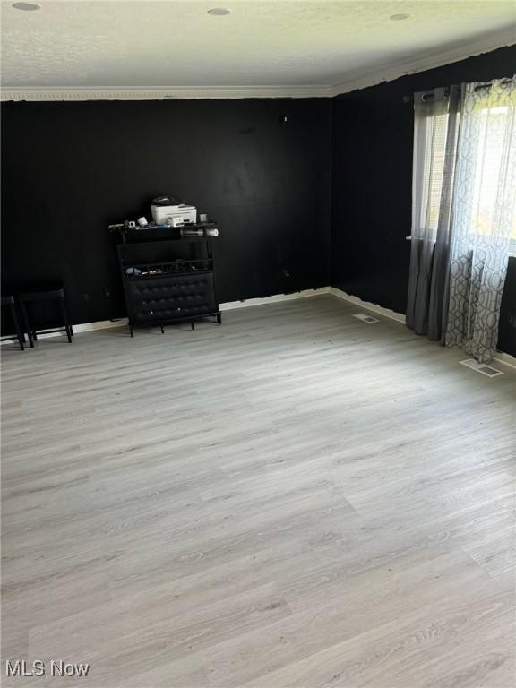 empty room featuring wood finished floors, visible vents, baseboards, and ornamental molding