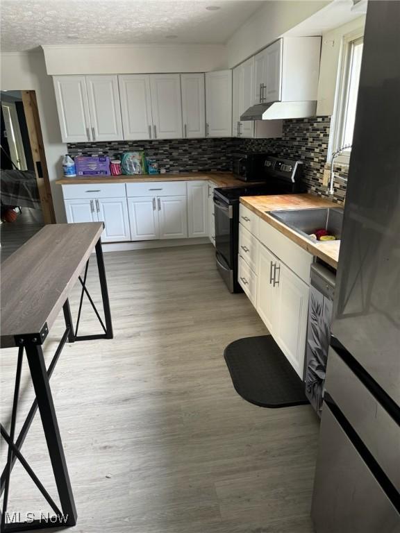 kitchen featuring black range with electric cooktop, light wood-type flooring, white cabinetry, decorative backsplash, and butcher block counters
