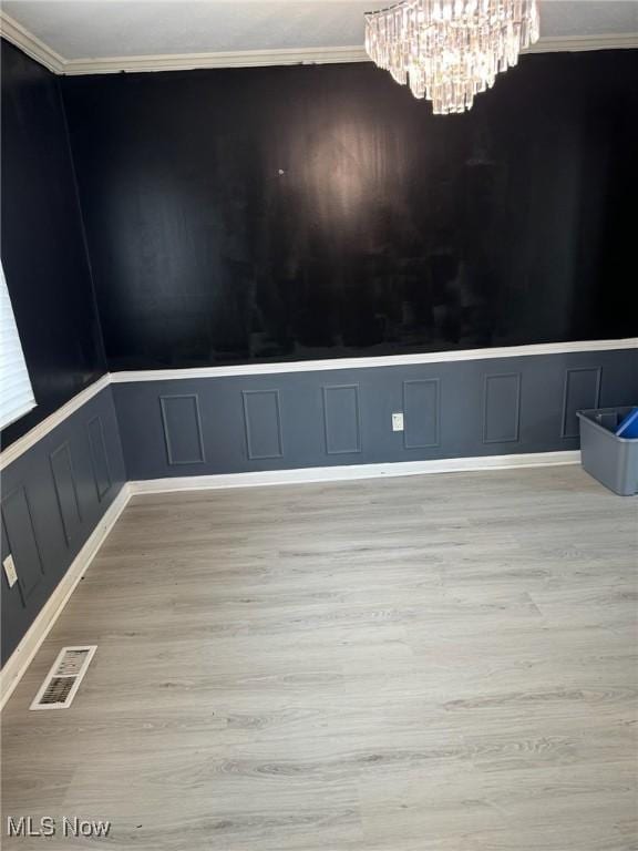 unfurnished room featuring a decorative wall, a notable chandelier, light wood finished floors, ornamental molding, and visible vents