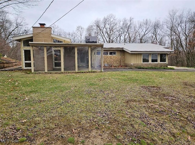 rear view of house featuring a chimney, a sunroom, and a lawn