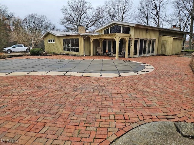 back of property with a chimney, a covered pool, a patio, and curved driveway