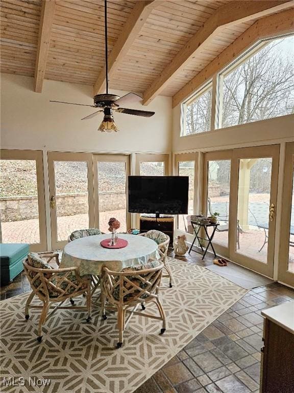 dining room featuring wooden ceiling, stone tile flooring, beam ceiling, a ceiling fan, and a high ceiling