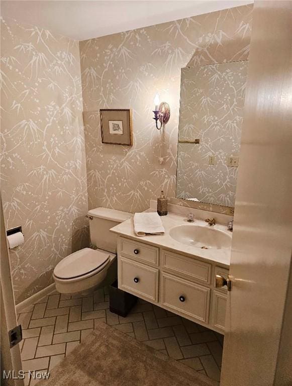half bath with toilet, vanity, and wallpapered walls