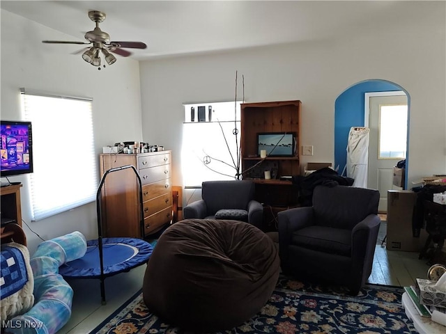 living area with arched walkways and a ceiling fan