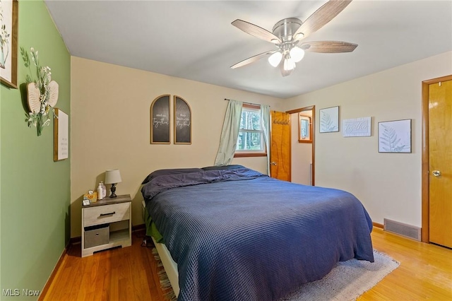 bedroom with wood finished floors, visible vents, a ceiling fan, and baseboards