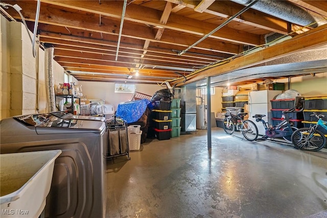 below grade area featuring heating unit, a sink, freestanding refrigerator, gas water heater, and washer and dryer
