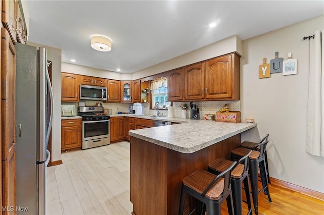 kitchen featuring decorative backsplash, a peninsula, brown cabinetry, appliances with stainless steel finishes, and a breakfast bar area