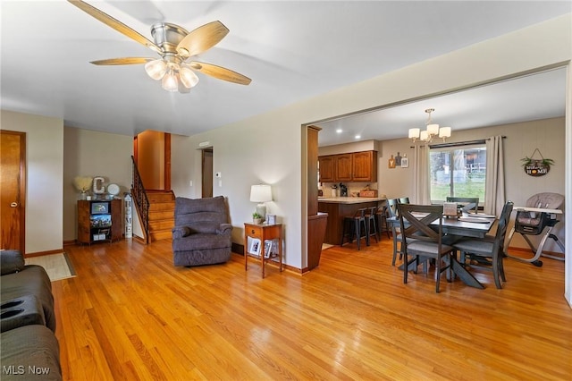 living room with stairway, baseboards, ceiling fan with notable chandelier, and light wood-type flooring