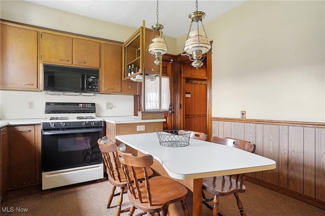 kitchen featuring brown cabinets, range with gas cooktop, light countertops, black microwave, and hanging light fixtures