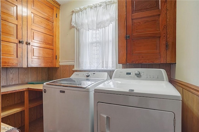 laundry area with wainscoting, wooden walls, independent washer and dryer, and cabinet space