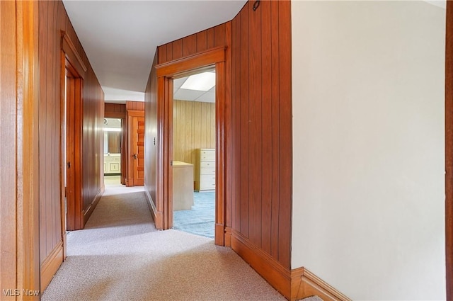 corridor with wooden walls, baseboards, and light colored carpet