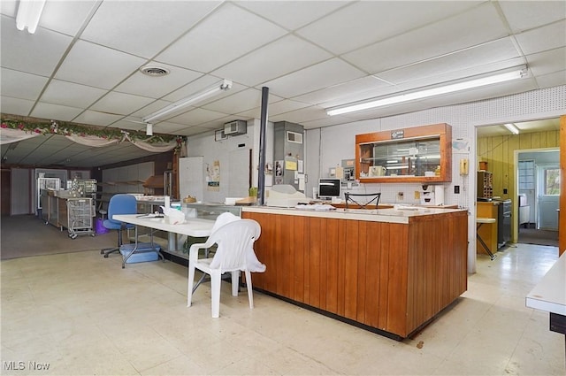 interior space featuring brown cabinetry, visible vents, a drop ceiling, and light floors