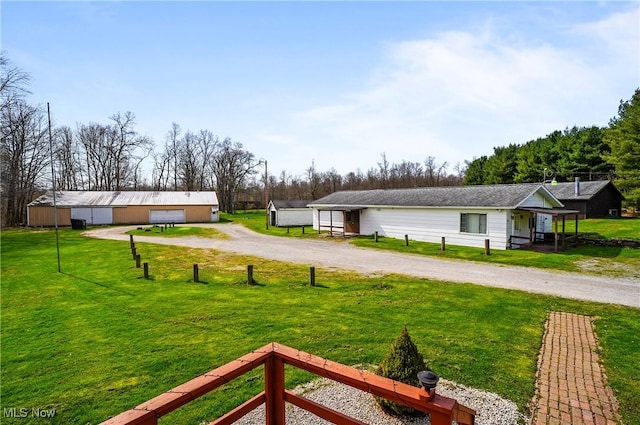 view of yard featuring an outdoor structure, a detached garage, dirt driveway, and a pole building