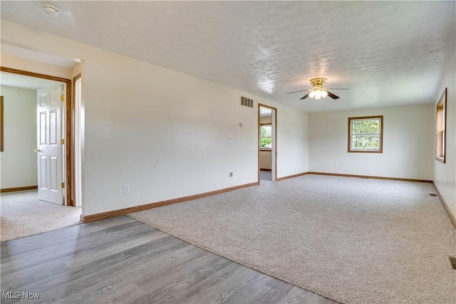 spare room featuring a ceiling fan, wood finished floors, a textured ceiling, baseboards, and visible vents