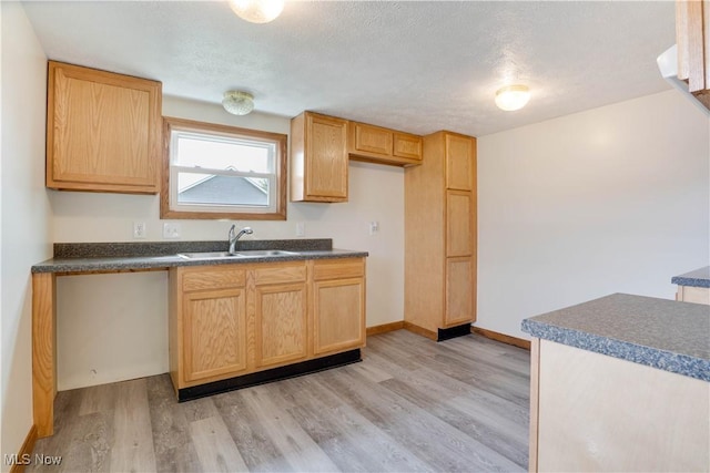 kitchen with dark countertops, light brown cabinets, a sink, light wood-type flooring, and a textured ceiling