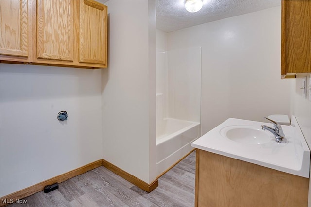 bathroom featuring a textured ceiling, shower / bathing tub combination, baseboards, wood finished floors, and vanity