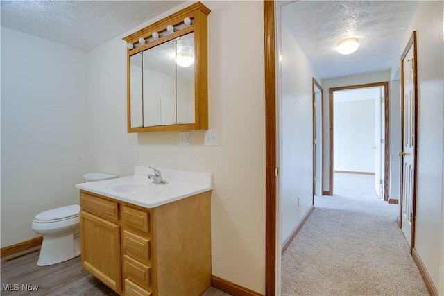 bathroom featuring a textured ceiling, vanity, baseboards, toilet, and visible vents