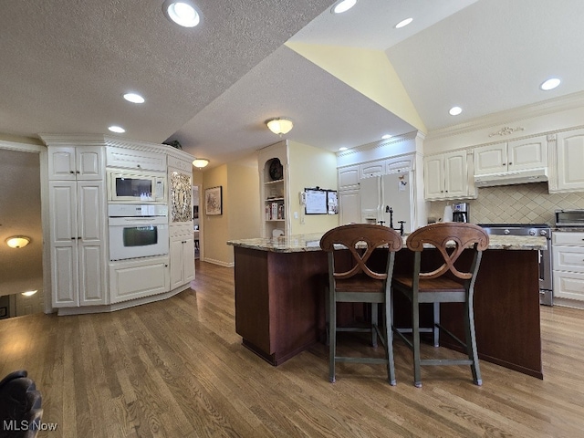 kitchen with white cabinets, under cabinet range hood, wood finished floors, and white appliances