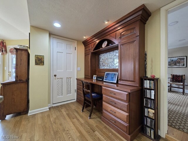 office space with a textured ceiling, built in desk, light wood-style floors, baseboards, and recessed lighting