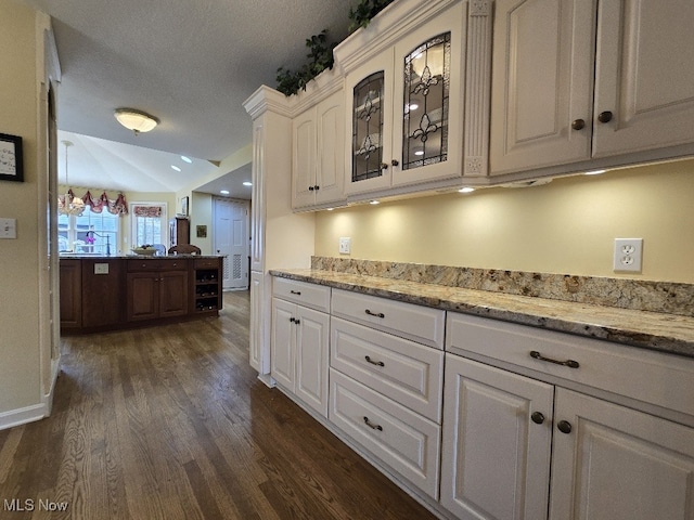 kitchen with glass insert cabinets, white cabinetry, light stone counters, and dark wood-style flooring