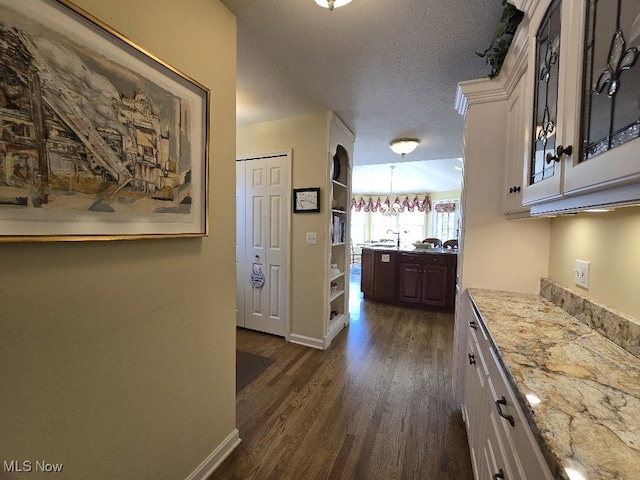 hallway featuring dark wood finished floors, baseboards, and a textured ceiling