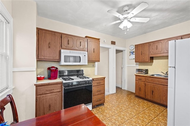 kitchen with a sink, white appliances, light floors, ceiling fan, and light countertops