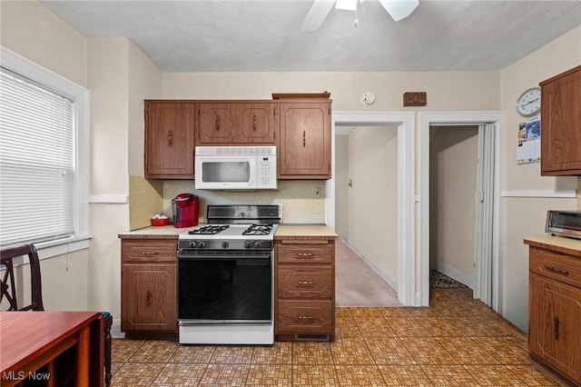 kitchen featuring range with gas cooktop, light floors, ceiling fan, white microwave, and light countertops