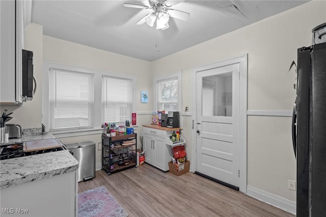 kitchen featuring light countertops, a ceiling fan, stainless steel microwave, freestanding refrigerator, and light wood-type flooring