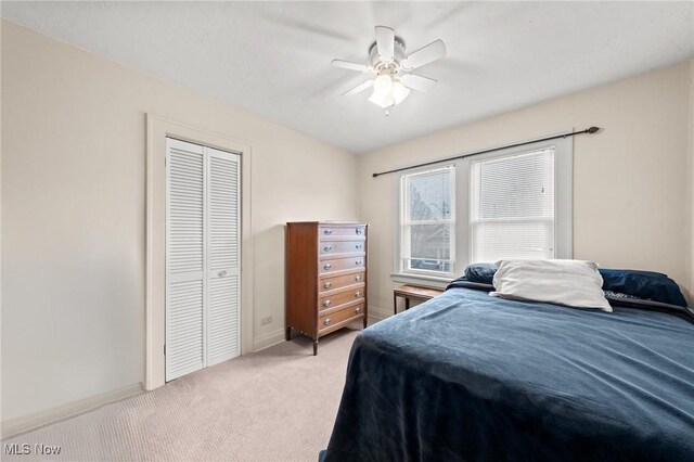 bedroom featuring ceiling fan, a closet, baseboards, and light carpet