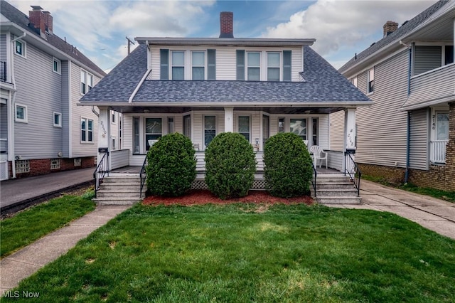 view of front of house with a shingled roof, a front yard, and covered porch