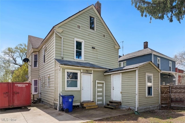 rear view of house with a chimney, fence, a patio, entry steps, and roof with shingles