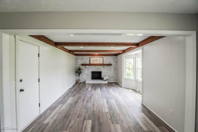 unfurnished living room with a fireplace, wood finished floors, beam ceiling, and baseboards